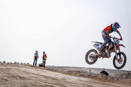 motorcross riding motorbike on sandy track during the day jumping