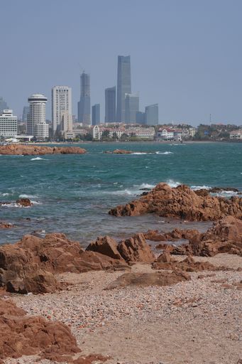 A vertical of modern skyscrapers on a rocky shore against the sea on a sunny day
