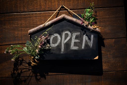 A black-colored sign with the word OPEN printed on it in white lettering is hung on a light-colored wooden wall