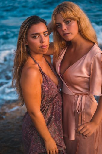 A couple of Caucasian girls posing in pink dresses during summer on the beach by the sea