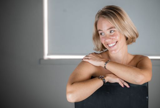 A young Caucasian woman in a black shirt, smiling and posing on a gray background