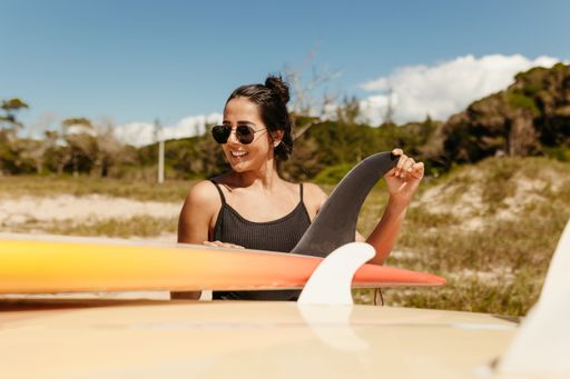 A young woman stands confidently beside her surfboard on a sun-drenched beach
