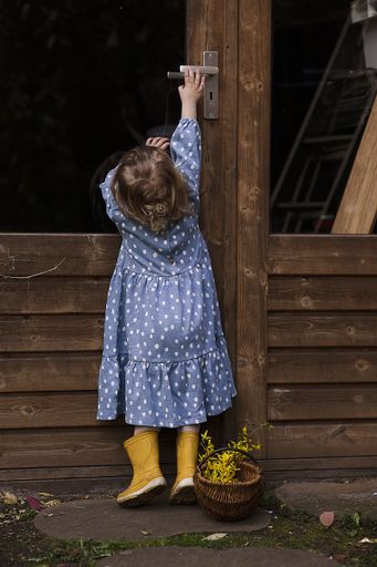 A vertical shot of a little girl wearing a blue dotted dress reaching for a barn door knob
