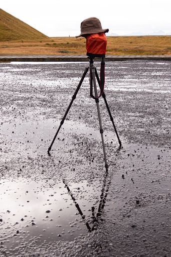 A creative shot of a brown bucket hat on a camera tripod on a wet ground