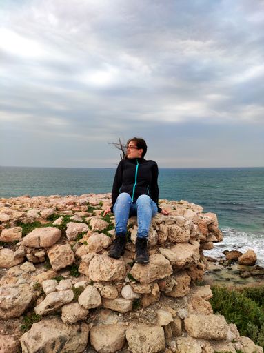 A young Israeli female sitting on rocks on background of the sea under the gloomy sky