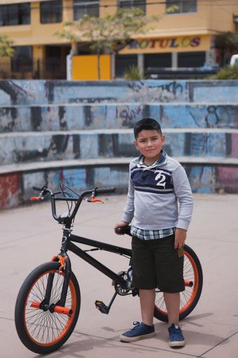 A hispanic smiling cute child standing at the park next to his bicycle