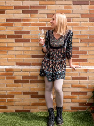A happy Spanish blonde woman with a glass of white wine leaning against a wall in the backyard of her house