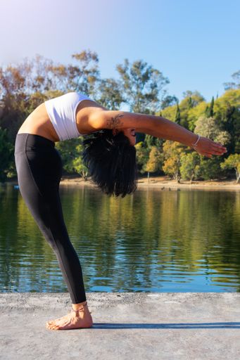A young Mexican yoga instructor woman doing yoga in the park near a lake