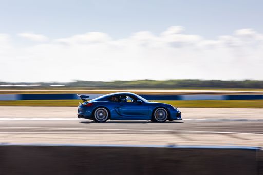 Blue Porsche Cayman GT4 racing at Sebring International Raceway through turn 15