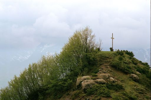 An isolated cross perched atop a rocky hillside, surrounded by lush trees in Abruzzo national park, Italy