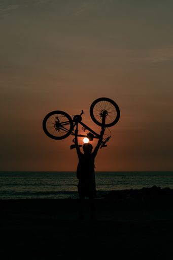 A silhouette of a biker carrying his bicycle at the beach during a beautiful sunset