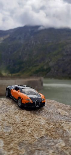 A small sports toy car parked atop a large, craggy rock formation, against a mountainous landscape