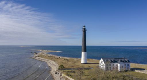 Aerial view to the historic lighthouse on on the daytime seascape with the long spit submerging into deep blue sea