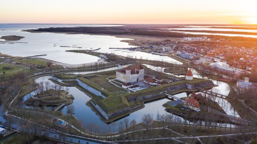Aerial view to the sunset colored coastal historic medieval fortress with the surrounding water front and bastions