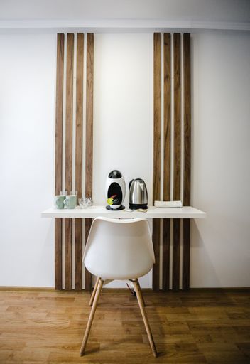A vertical shot of a white chair in front of a table with no legs with glasses, mugs, coffee machine, electric kettle