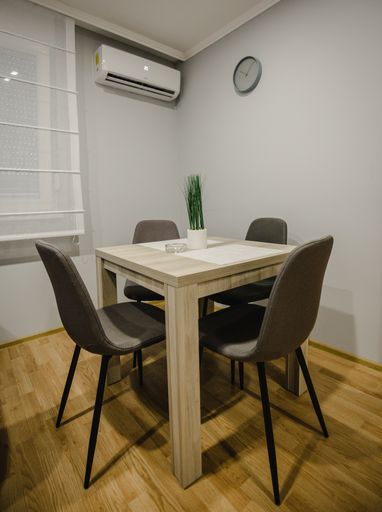A vertical shot of a wooden table with chairs in a room with an AC and wall clock