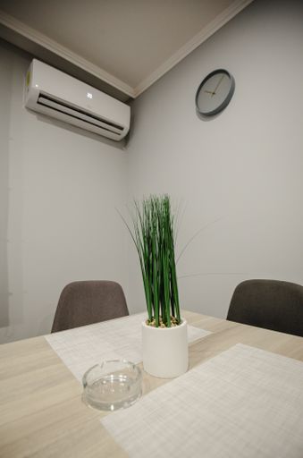 A vertical shot of a plant and ashtray on a wooden table in a room with chairs, AC, and wall clock