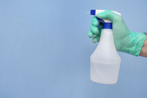 A gloved hand holding a water disperser for cleaning isolated on a blue background