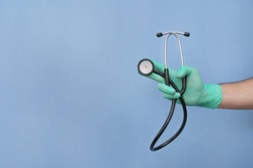 A gloved hand of a doctor holding a stethoscope isolated on a blue background