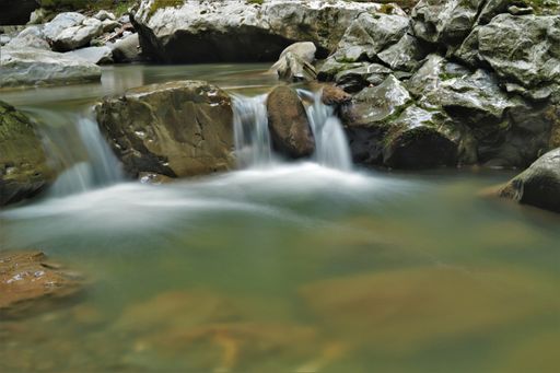 The cascades of a fast-flowing stream running through mountain rocks into the river - vertical shot