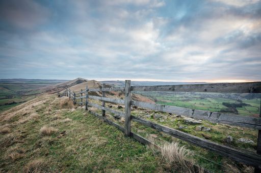 A shot of the wooden fence on the green hills during cloudy weather