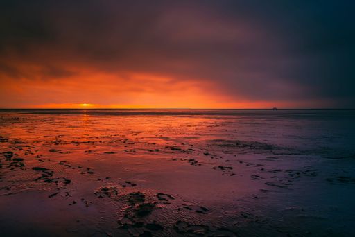 A scenic view of a sandy beach against the sea at red sunset