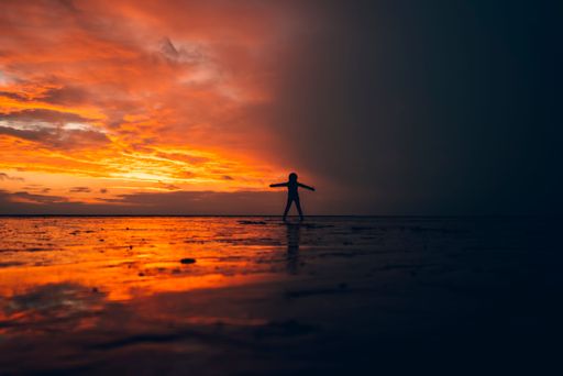 A silhouette of a person standing in shallow water against the sea at orange sunset