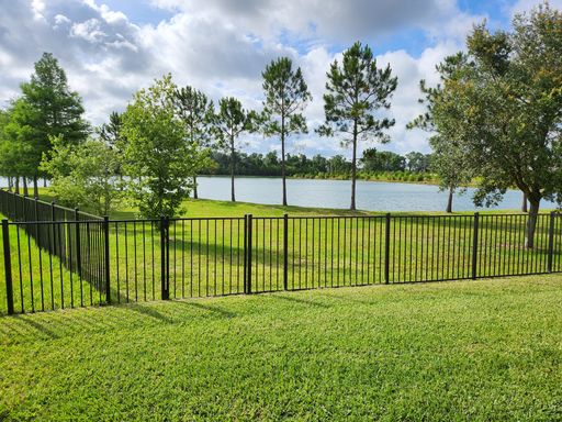 A sunny day in a park features a tranquil pond with a black fence and green trees.