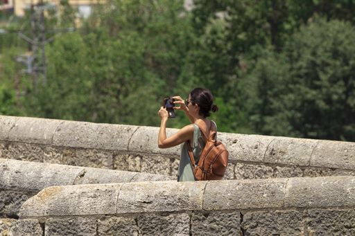 young woman taking a photo with the mobile from a medieval bridge in besalu in girona, spain