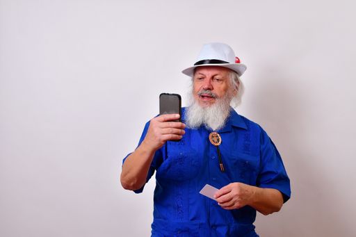 A mature gentleman doing online shopping using his cell phone and a credit card isolated on a white background