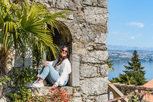 An adult woman sitting on a castle with the sea in the background on a sunny day in Croatia