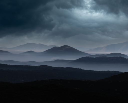 Dramatic landscape of rocky mountains shrouded in dark, cloudy skies with a gray overcast