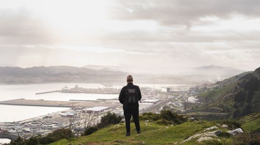 An adult backpacker standing on a hill and looking at the sea under the sunlight in Spain