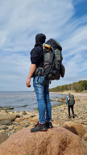 A male figure with a backpack atop a large rock on the shoreline of an ocean
