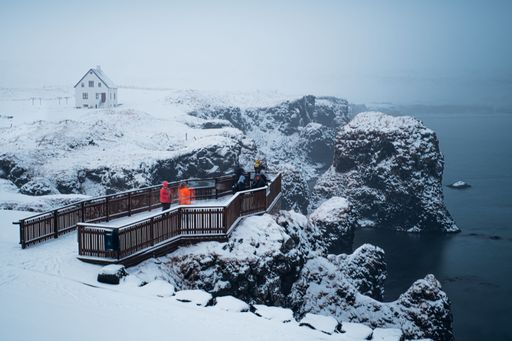 A majestic winter landscape featuring a snow-covered cliff and a white house located in the background in Reykjavik