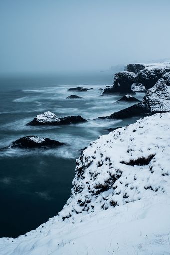 A picturesque winter landscape in Reykjavik, Iceland featuring a snow-covered lake and a rocky outcropping on the shore