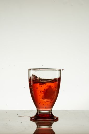 A vertical shot of a glass of red, splashing drink isolated on a reflective surface