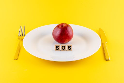 A closeup of wooden blocks with SOS phrase and an apple on a white plate with a knife and fork
