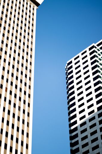 A vertical shot of two modern office buildings with white walls and black windows under the sunlight