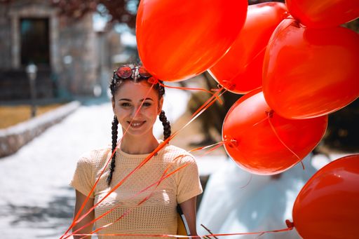 A shallow focus of a cheerful and beautiful brunette female holding red heart-shaped balloons