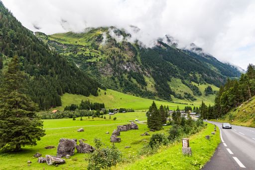 Road in the mountains covered with green forest under white clouds