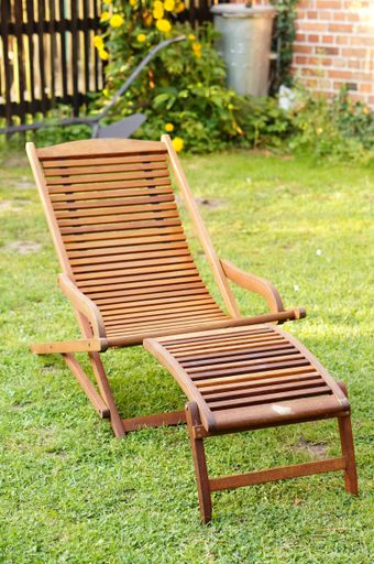A vertical picture of an outdoor wooden chair in a garden surrounded by greenery