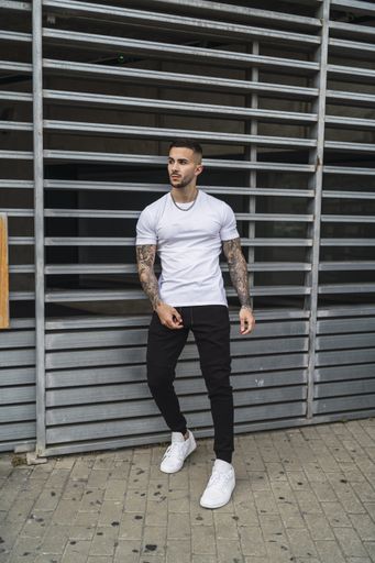 A vertical shot of a young European man with tattooed arms leaning on a gat