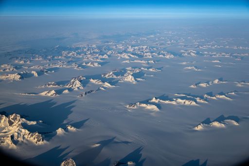 An aerial view of a vast, snow-covered mountain range, visible through the window of an airplane