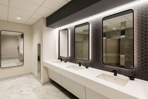 A modern bathroom with three white porcelain sinks lined up against a mirrored wall.