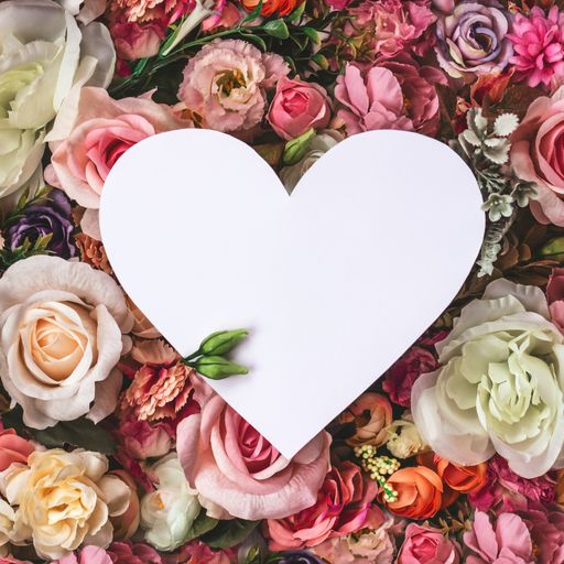 Beautiful colorful flowers wall background, with white heart greeting card with copy space; Spring, wedding, anniversary or florist greeting card