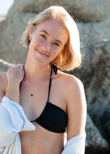 A portrait of a blonde girl with short hair and in a black bikini on the background of the boulder at the beach