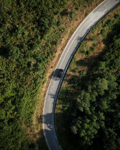 An aerial shot of a black car on a country road in Portugal surrounded by green lush trees