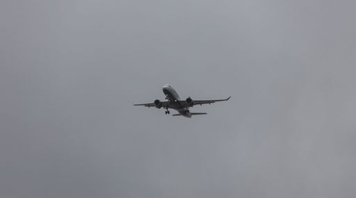 A JetBlue Airbus A220 aircraft flying through the sky on a grey cloudy day
