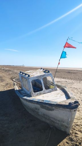 A vertical shot of an abandoned old boat on the sandy beach under the blue sky